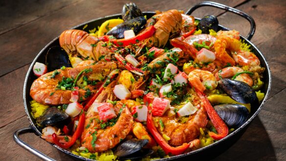 Плато з паельї з морепродуктами, включає креветки, мідії, шматочки крабового м'яса, приправлене свіжою зеленню та перцем на яскравому рисовому фоні.