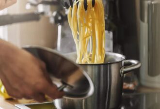 Процес варіння спагеті в каструлі на кухонній плиті, з піднятою кришкою та виделкою для макаронів
