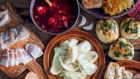Традиційна українська кухня з тарілками вареників, борщу, салом, хлібом та домашніми пиріжками, оформлена на дерев'яному столі.