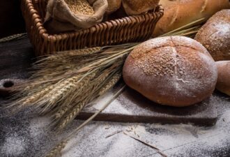 Свіжий хліб на дерев'яному столі, оточений снопами пшениці та мукою, у кошику із зерном.