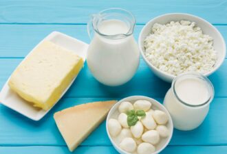 Асортимент молочних продуктів на блакитному фоні: натуральне молоко в графині, сир, творог, моцарела і шматок твердого сиру. Ідеально для здорового харчування та смачних страв.