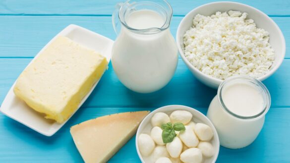 Асортимент молочних продуктів на блакитному фоні: натуральне молоко в графині, сир, творог, моцарела і шматок твердого сиру. Ідеально для здорового харчування та смачних страв.
