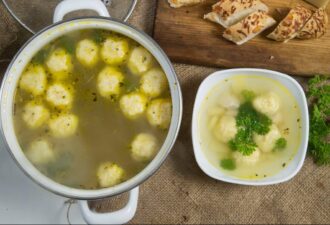 Смачний курячий бульйон з кльоцками, поданий у двох тарілках: одна з основною стравою, інша - з порцією бульйону та зеленню. На фоні - свіжий хліб. Ідеально для домашнього обіду.