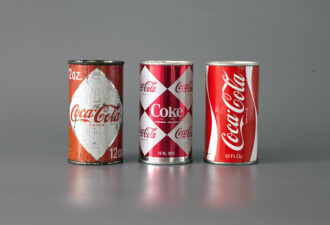 Три бляшанки Coca-Cola різних дизайнів: стара бляшанка з червоним дизайном, бляшанка з комбінацією червоно-білого кольору та класична версія з білим логотипом на червоному фоні.