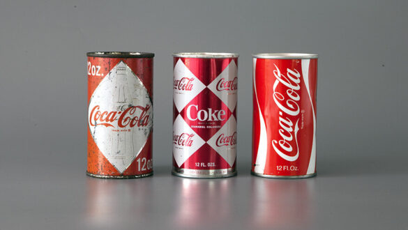 Три бляшанки Coca-Cola різних дизайнів: стара бляшанка з червоним дизайном, бляшанка з комбінацією червоно-білого кольору та класична версія з білим логотипом на червоному фоні.