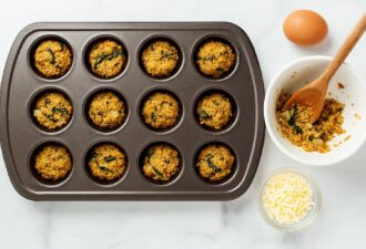 Форма для мафінів, заповнена сирими овочевими кульками з кіноа та шпинатом, поруч інгредієнти — яйце, тертий сир і миска з начинкою — готується здорова страва.