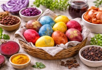 Великодні яйця, пофарбовані натуральними барвниками (буряк, куркума, капуста, кава), у кошику на дерев’яному столі з інгредієнтами для фарбування навколо