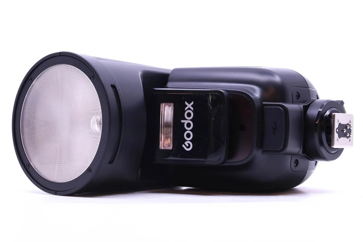 Фотоспалах Godox крупним планом — зовнішній спалах Godox, знятий збоку на світлому фоні, з великим круглим розсіювачем.